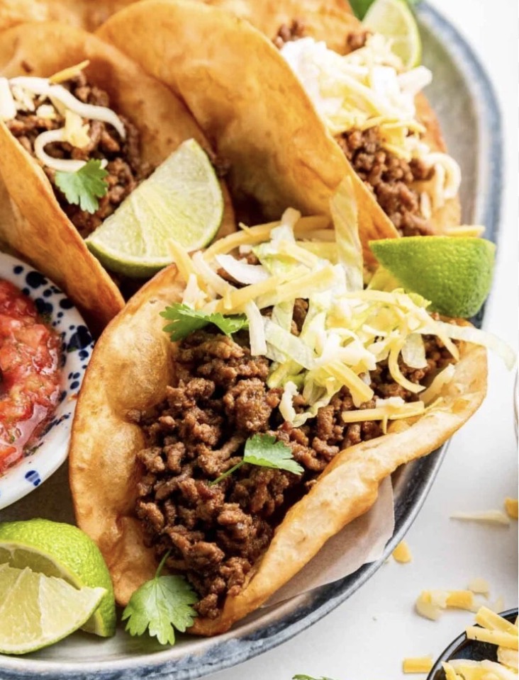 Crispy beef tacos topped with lettuce and cheddar with lime wedges